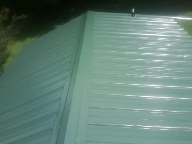 New green metal panels meeting at the ridge of a roof — Flat Roof Repair work by our crew in Fairmount